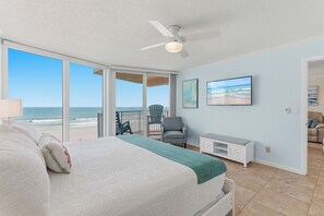 Ein Schlafzimmer mit Bett, Deckenventilator, Blick auf den Strand, Stuhl und Fernseher.