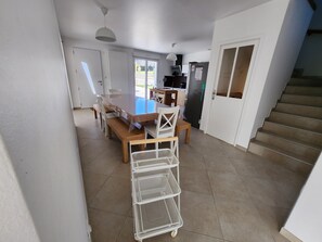 Et rummeligt køkken med et spisebord, stole, et køleskab og en trappe til et andet plan.