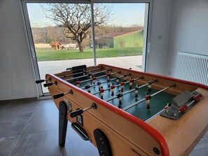 A foosball table in a room with a large window, a radiator, and a door. - Holiday Home 'Gîte Rural Le Vendangeoir' with Private Garden and Wi-Fi (Colombé-la-Fosse)