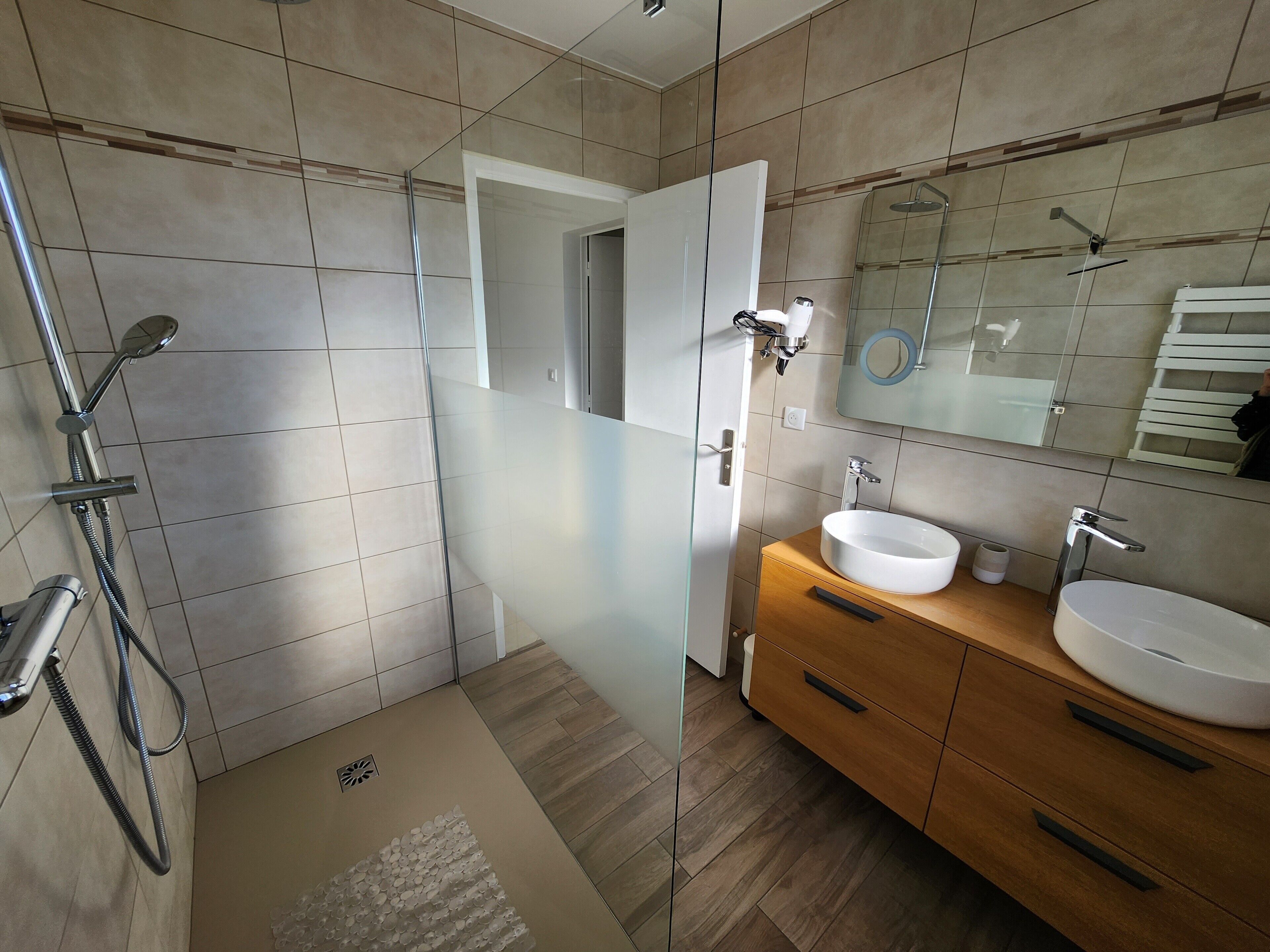 Un baño moderno con cabina de ducha de vidrio, tocador de madera con lavabo y un espejo grande.