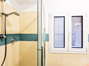 Ducha con cabezal de ducha de mano, puerta de cristal y ventana con vistas al exterior.