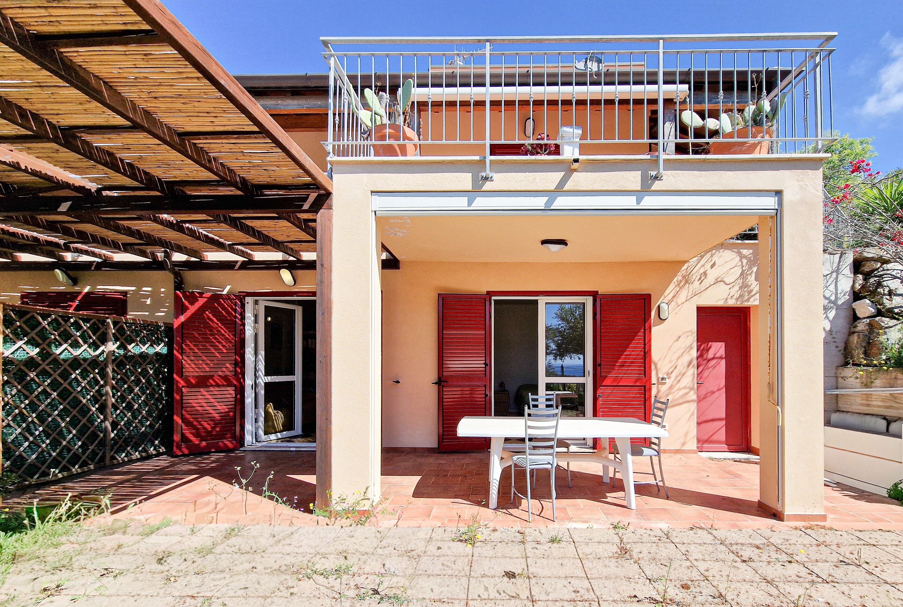 Ein zweistöckiges Gebäude mit Balkon, Tisch und Stühlen draußen sowie einer roten Tür.