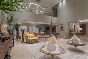 A spacious lobby with a high ceiling, modern furniture, and hanging chairs.