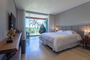 Una habitación de hotel moderna con una cama grande, un escritorio, una silla, un televisor y un balcón con vistas a palmeras.