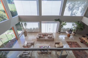 Un amplio salón con un ventanal grande, un sofá color beige, una mesa de centro y plantas en macetas.