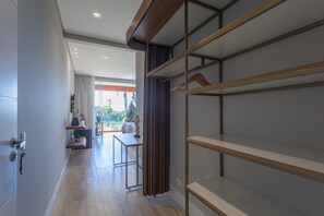 Una habitación de hotel moderna con suelo de madera, un ventanal con cortinas, un armario empotrado y una pequeña zona de estar con una mesa y sillas.