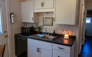 A kitchen with white cabinets, a black countertop, a sink, a microwave, a plant, and a framed picture on the wall.
