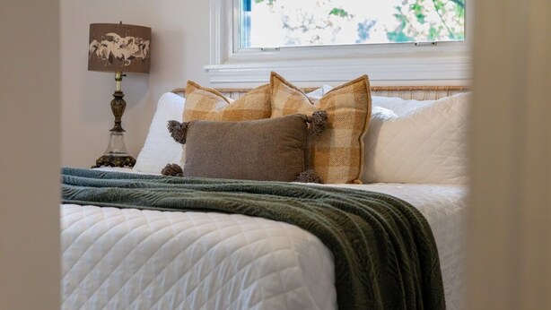 Uma cama bem arrumada com edredom branco acolchoado, manta verde e vários travesseiros com diferentes estampas e cores.