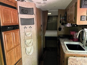 Une cuisine compacte pour camping-car, avec des placards en bois, un four à micro-ondes, un évier et un petit lit.