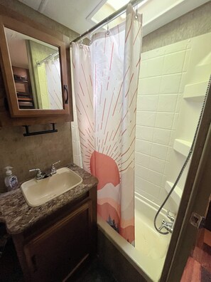 Une salle de bain équipée d’un lavabo, d’un miroir, d’un rideau de douche et d’une baignoire.