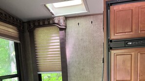 Eine kompakte Küchenzeile für ein Wohnmobil, mit integriertem Kochfeld, Spüle, einem Fenster mit Jalousien und einer Sitzbank.