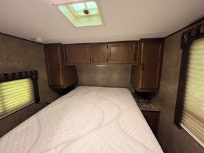 A bedroom with a skylight, a bed with a patterned bedspread, wooden cabinets, and a window with blinds.