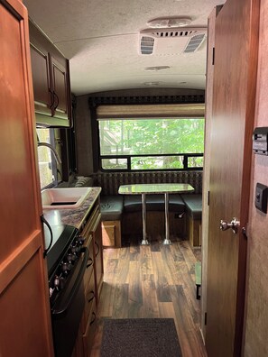 A compact RV kitchen with a stove, sink, and a dining area with a bench.