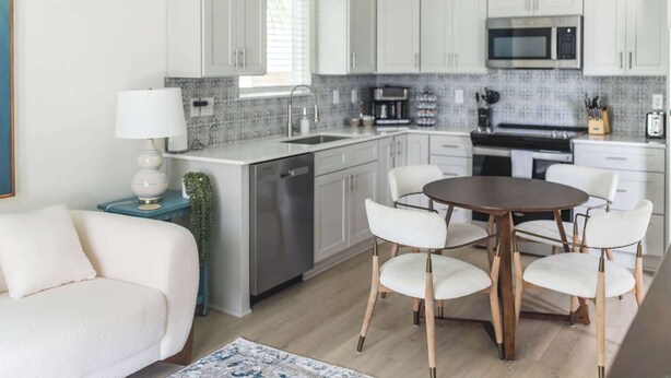 Una cucina moderna con mobili bianchi, una lavastoviglie in acciaio inossidabile, un forno a microonde e un'area pranzo con un tavolo rotondo e sedie bianche.