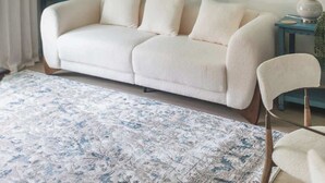 Un soggiorno con un grande quadro, un divano bianco, un tappeto blu e una ventola a soffitto.