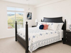 Ein Schlafzimmer mit Himmelbett, Nachttisch, Lampe, Gemälde und Fenster mit Landschaftsblick.