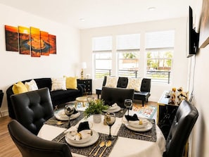 A living room with a dining area, black leather sofas, a table set for four, and a large window with blinds. - Walk to Temple Square | Stylish SLC Getaway (Salt Lake City)