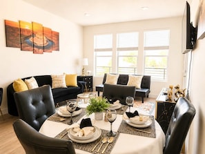 A living room with a black leather sofa, a dining table set for four, and a large window with blinds. - Walk to Temple Square | Stylish SLC Getaway (Salt Lake City)