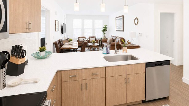 Una cocina moderna con una isla central, armarios de madera, lavavajillas y un comedor con sofá y sillas.