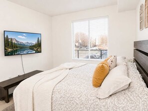 Ein Schlafzimmer mit Bett, Fernseher, Fenster und Blick auf einen See und Berge.