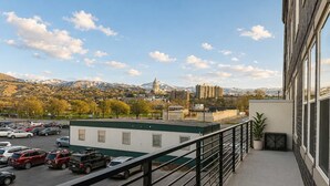 Un balcón con vista a un estacionamiento, un edificio con techo verde y montañas al fondo.