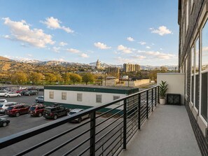 Ein Balkon mit Blick auf einen Parkplatz, ein Gebäude mit einer Dachbegrünung und Berge im Hintergrund.
