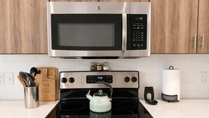A kitchen with a stainless steel microwave, a stove with a kettle, and wooden cabinets. - 2BR Urban Oasis in Downtown SLC - Sleeps 6, Gym (Salt Lake City)