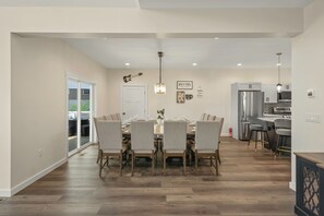 Eine moderne Küche mit einem Edelstahl-Kühlschrank, eine Essecke mit einem Holztisch und gepolsterten Stühlen sowie ein Flur mit einer Schiebeglastür, die auf eine Außenpatio führt.