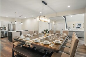 Een moderne eetkamer met een lange houten tafel, gedekt voor een maaltijd, omringd door comfortabele stoelen.