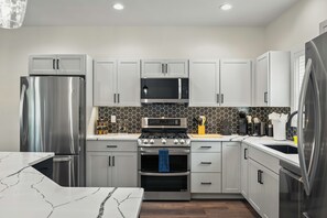 Et moderne køkken med stålemmer, hvide skabe og en backsplash i sort hexagonmønster.