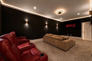 A home theater room with a red leather couch, a beige sofa, and a wall-mounted TV displaying 'NETFLIX'. - The South Harmony House, Luxury Escape, HotTub, 5,000sqft, Gameroom (Lake Harmony)