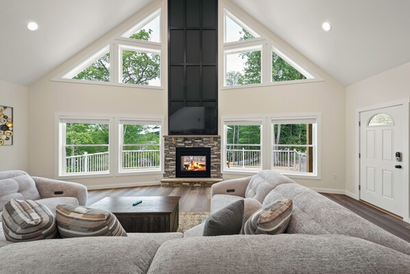 A spacious living room with a fireplace, large windows, and a high ceiling. - The South Harmony House, Luxury Escape, HotTub, 5,000sqft, Gameroom (Lake Harmony)