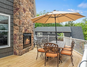 An outdoor deck with a stone wall, a fireplace, and a table with chairs. - The South Harmony House, Luxury Escape, HotTub, 5,000sqft, Gameroom (Lake Harmony)