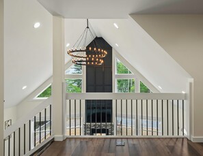 Een ruime kamer met een hoge plafond, een open haard en een groot raam met uitzicht op een terras.