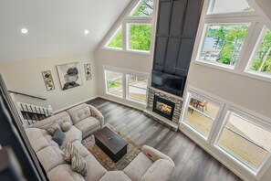 Amplia sala de estar con techo alto, chimenea y grandes ventanales con vistas al exterior.