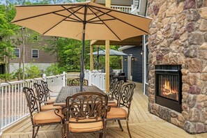 Eine Terrasse im Freien mit Tisch und Stühlen, einem Kamin aus Stein und Blick auf ein Haus.
