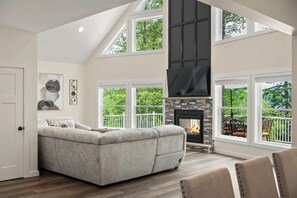 A spacious living room with a fireplace, large windows, and a high ceiling. - The South Harmony House, Luxury Escape, HotTub, 5,000sqft, Gameroom (Lake Harmony)