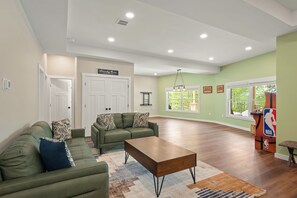 A spacious living room with a sectional sofa, a coffee table, and a large window providing natural light. - The South Harmony House, Luxury Escape, HotTub, 5,000sqft, Gameroom (Lake Harmony)