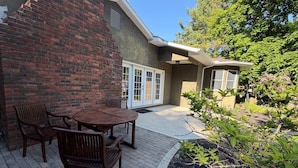 A patio with a brick wall, a wooden table and chairs, and a garden area with various plants. - Dublin's Private Ranch Retreat (Delaware)