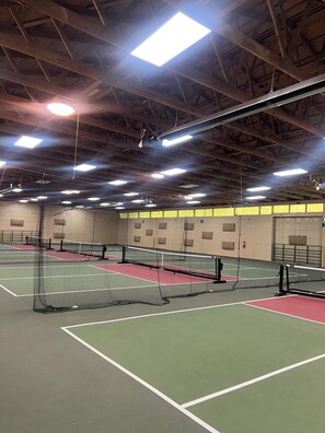 An indoor tennis court with multiple courts, netted areas, and overhead lighting.