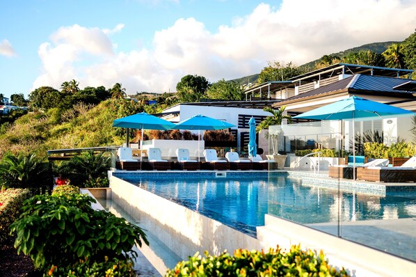 A swimming pool with lounge chairs and umbrellas, surrounded by greenery and a hillside.