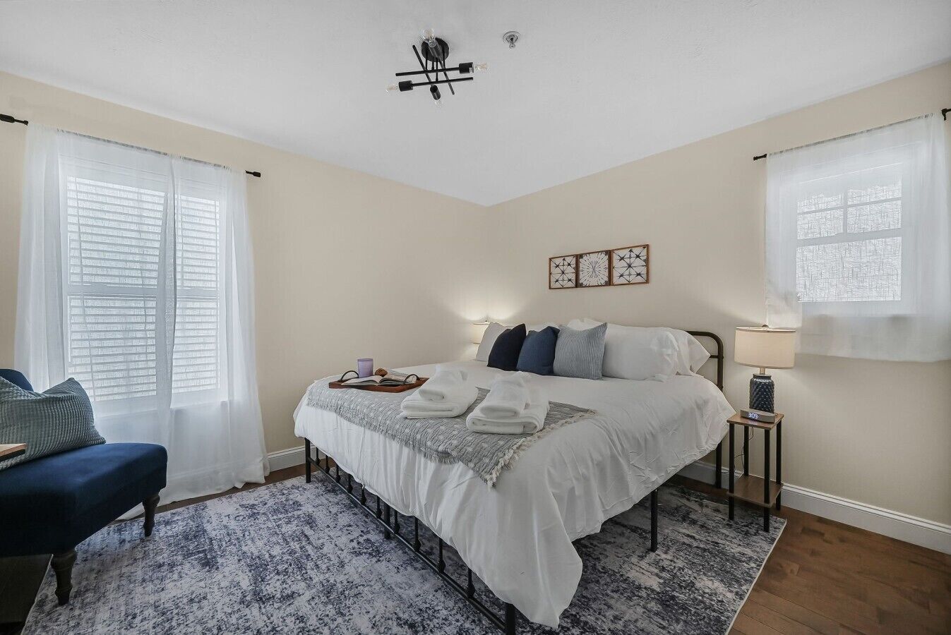 A bedroom with a bed, bedside table, lamp, curtains, and a view of the outside.