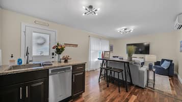 A modern kitchen with a dishwasher, a dining area with a bar stool, and a living room with a TV.