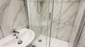 Ein Badezimmer mit einer gläsernen Duschkabine, einem weißen Waschbecken und Wänden mit Marmor-Muster.