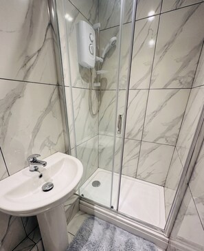 A bathroom with a glass-enclosed shower, a white sink, and marble-patterned walls. - Vibrant Central One bedroom
67PRE01 (Brighton and Hove)
