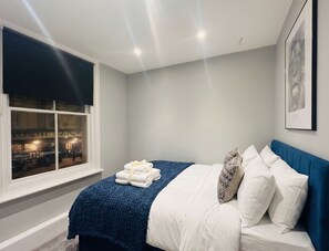 A bedroom with a bed, a window, and a wall-mounted picture. - Vibrant Central One bedroom
67PRE01 (Brighton and Hove)