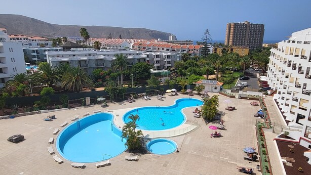 Uma piscina grande ao ar livre, com vários espreguiçadeiras e algumas pessoas.