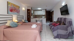 Quarto de hotel com duas camas, um sofá, uma televisão e uma área de cozinha.