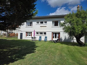 A two-story building with a flat roof, a balcony, and a patio area with outdoor furniture.