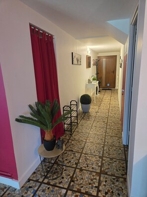 A hallway with a tiled floor, a potted plant, a small table, and a door at the end.